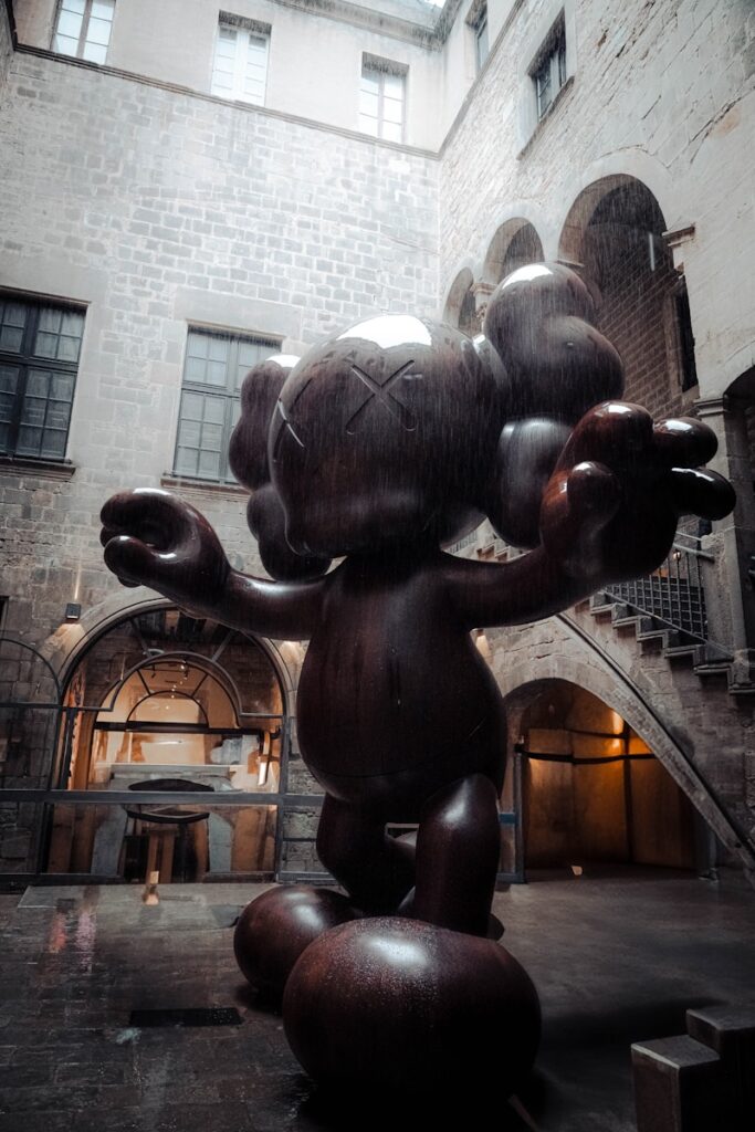 A large kaws sculpture stands in a courtyard.